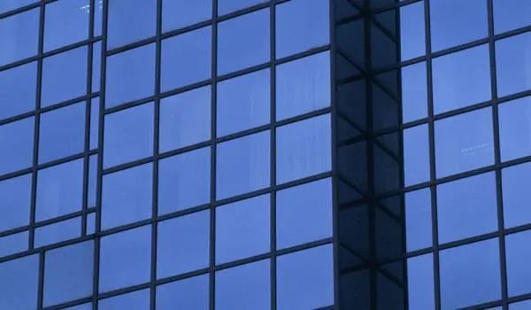 A close-up of a blue glass-clad building facade showing the pattern of windows and a protruding architectural feature.