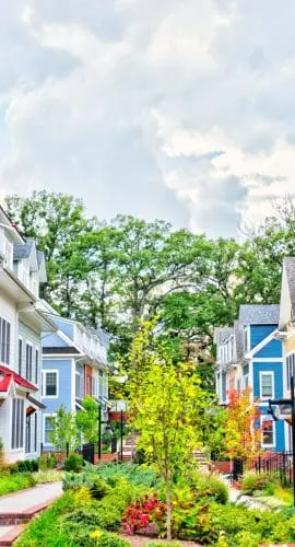 A row of colorful suburban townhouses with front porches and a landscaped pathway under a partly cloudy sky.