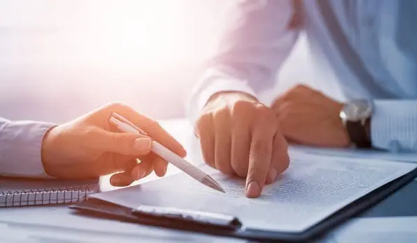 A person is reviewing a document with a pen in hand, ready to write or make annotations.