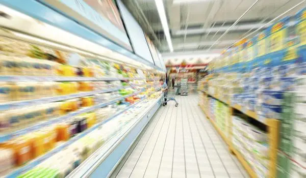 A blurred view of a supermarket aisle with products on shelves and bright lighting, conveying a sense of motion or haste.