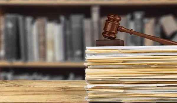 A wooden gavel rests on a stack of papers with a blurred backdrop of bookshelves.