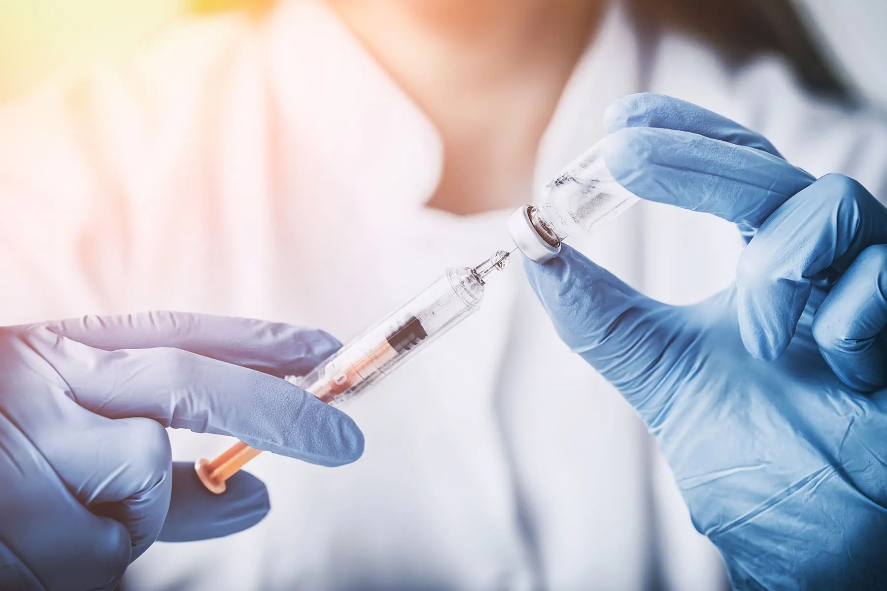 A healthcare professional is preparing a syringe for vaccination, wearing gloves and working under bright lighting.