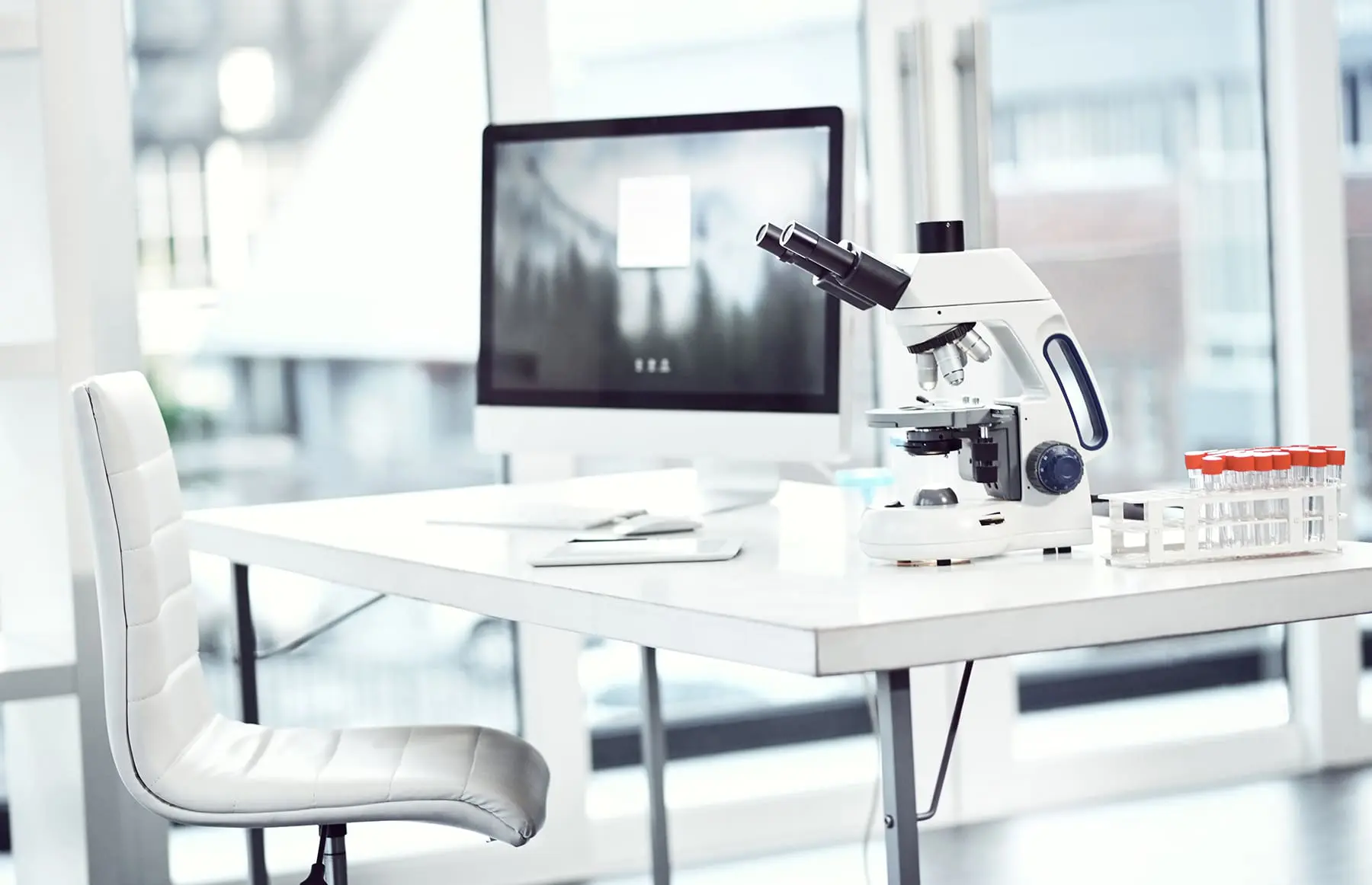 A modern laboratory setup with a microscope, computer monitor, and other scientific equipment on a clean desk.