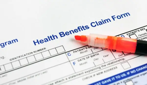 A health benefits claim form is partially filled out with a pen resting on top.