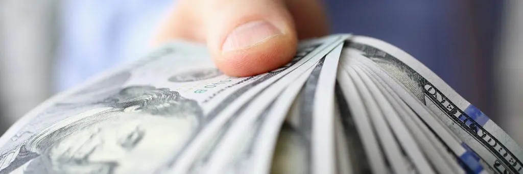 A hand is holding a fanned-out stack of US dollar bills.