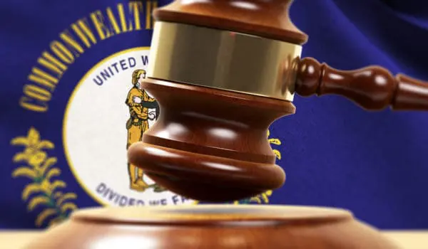 A wooden gavel is poised above a sounding block against a backdrop featuring a seal emblem.