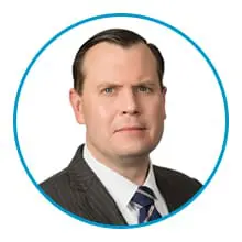 A man in a suit and tie is framed within a blue circle.