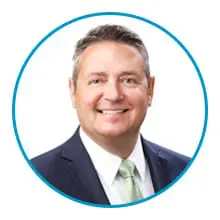 A man in a suit and tie is smiling within a blue circular border.