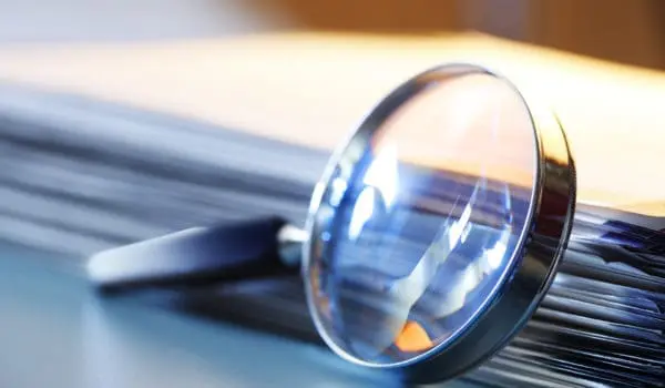 A magnifying glass leans against a thick stack of papers. Photographed with a very shallow depth of field.