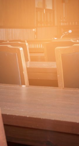 Empty wooden chairs and desks are basking in the warm glow of sunlight, suggesting a peaceful setting, perhaps in a lecture hall or courtroom.