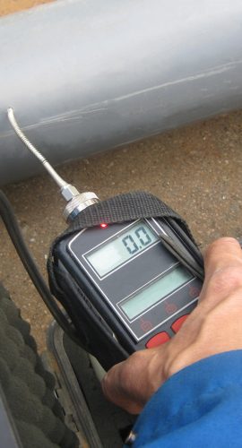 A person's hand is holding a digital tire tread depth gauge against a tire to measure its tread depth.