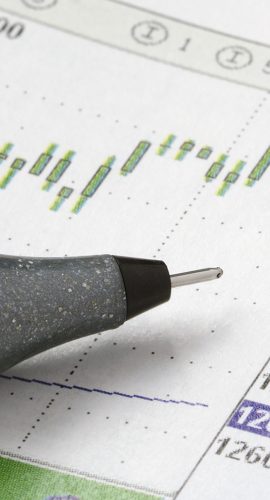 A silver pen is resting on a printed financial report with line and bar graphs.