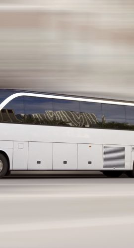 A white coach bus is in motion with a blurred background conveying the sense of speed.