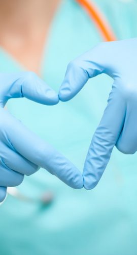 A healthcare professional wearing blue gloves is forming a heart shape with their hands.