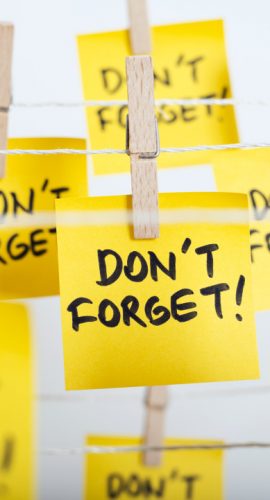 Multiple yellow sticky notes with "DON'T FORGET!" written on them are attached to a string by wooden clothespins.