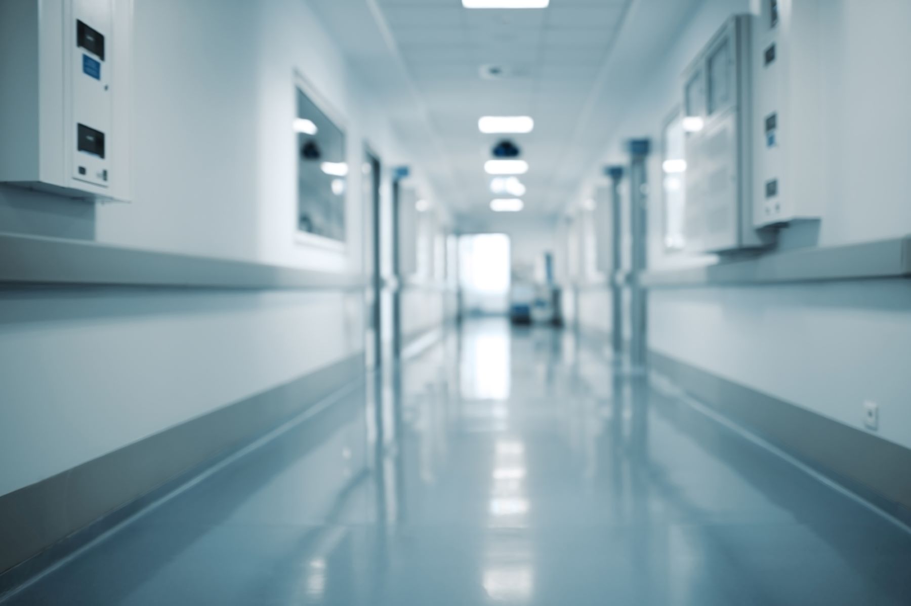 A blurry perspective of a hospital corridor with clinical blue tones and a figure in the distance.