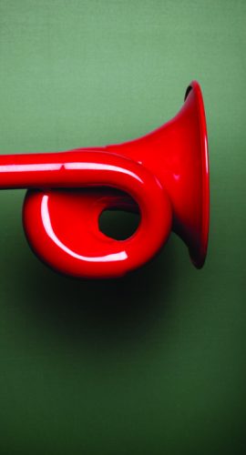 A red megaphone is held close to a person's ear against a green background.