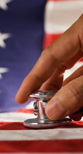A hand holding a stethoscope rests on an American flag.