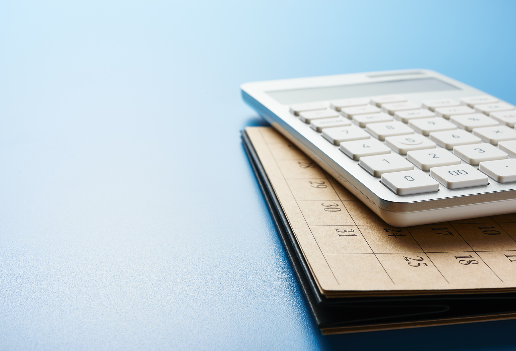 A calculator rests on top of a notebook against a blue background.