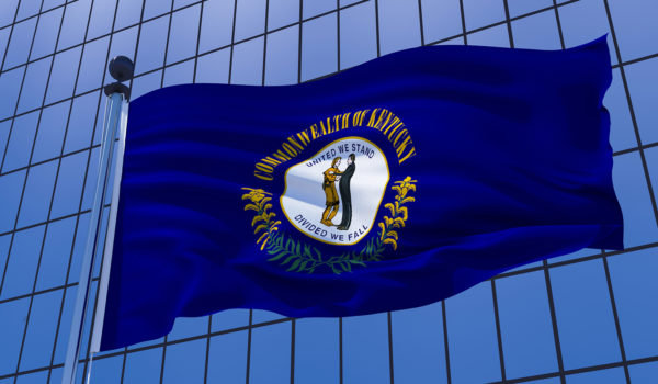 A Kentucky state flag is waving in front of a glass building.