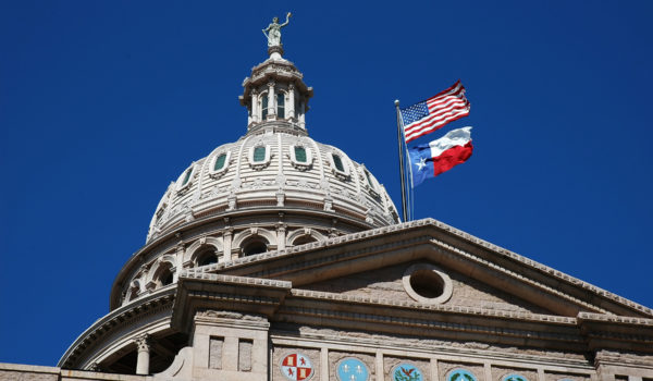 A grand architectural dome features a prominent American flag and another flag set against a clear blue sky.