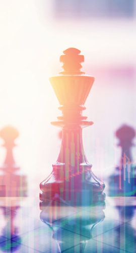 Several chess pieces are arranged on a reflective surface, with a prominent king piece in focus and a bright, abstract background.