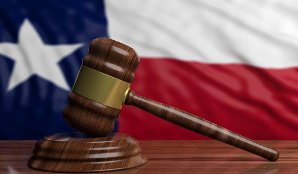 A gavel rests on a wooden table in front of a Texas flag.