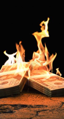Closeup heap of Dollar bills burning with orange fire on rough cracked ground against black background as symbol of inflation economic collapse. 3d render
