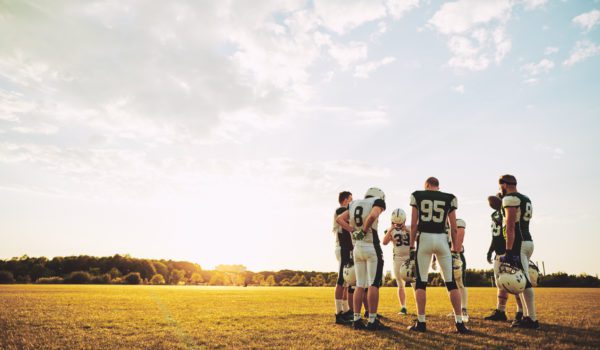 Group of young American football players standing together in a circle on a sports field talking strategy