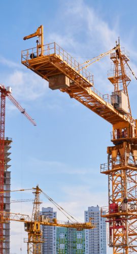 several construction tower cranes of different heights at a building site during the construction of blocks of flats, view against the sky