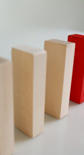 Close-up of one red wooden block stop other ones from falling like dominoes, domino effect. Risky and business strategy, planning, danger, fail concept