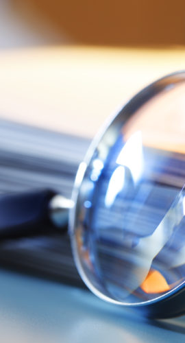 A magnifying glass leans against a thick stack of papers. Photographed with a very shallow depth of field.
