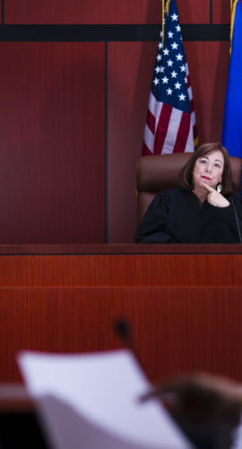 Stock photo of a judge in her sixties watching an attorney explain papers to a defendant.